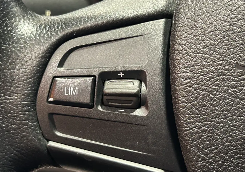 Gros plan sur les commandes de limitation de vitesse sur le volant en cuir noir d'une BMW Série 1 gris diesel de 2014.