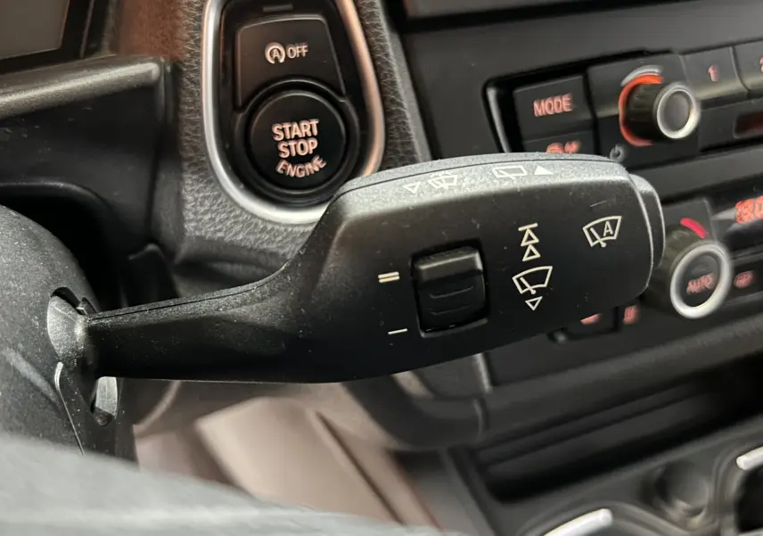 Gros plan sur la commande d’essuie-glace et le bouton Start/Stop du tableau de bord d’une BMW Série 1 gris 2014.