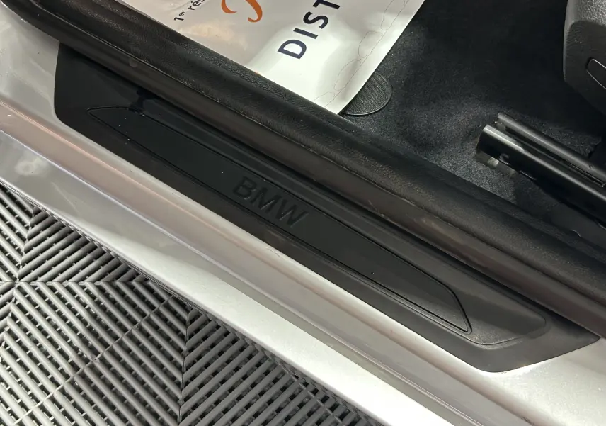 Gros plan sur la marche d'entrée noire avec logo BMW sur le côté gauche d'une BMW Série 1 gris 2014.