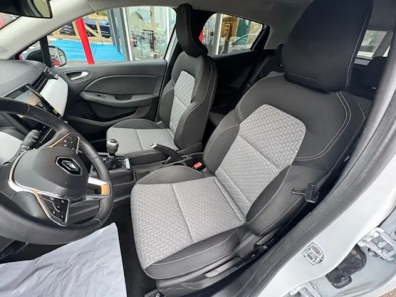 Vue intérieure côté conducteur de la Renault Clio blanc glacier 2023, sièges tissu gris à motif 3D et volant multifonction.