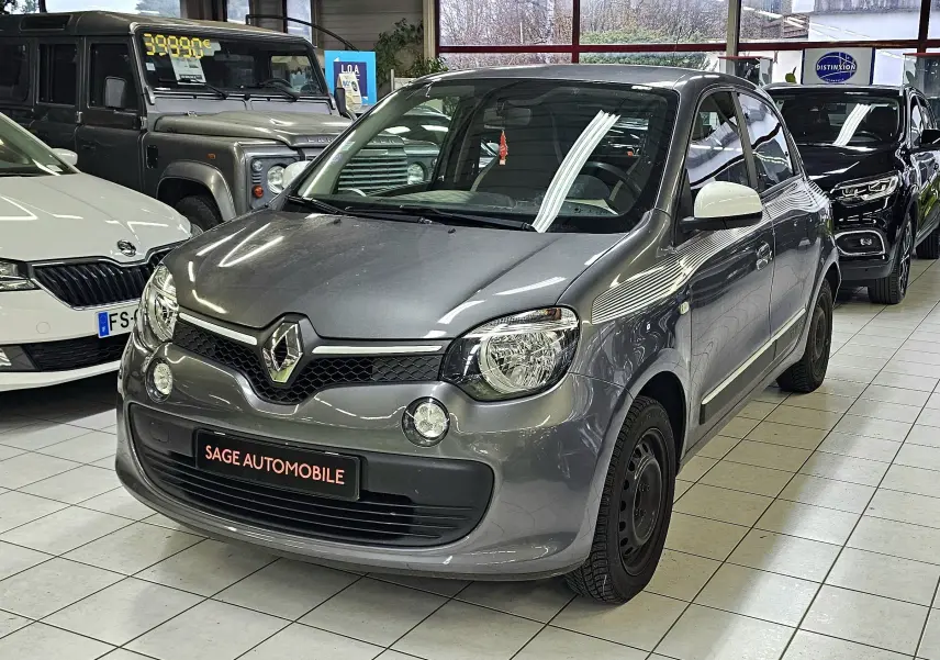 Renault Twingo III gris lunaire vue 3/4 avant droit en intérieur avec rétroviseurs blancs et jantes noires.