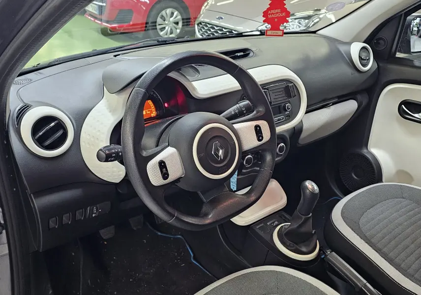 Vue intérieure côté conducteur de la Renault Twingo III gris lunaire 2018, volant et tableau de bord avec console centrale.