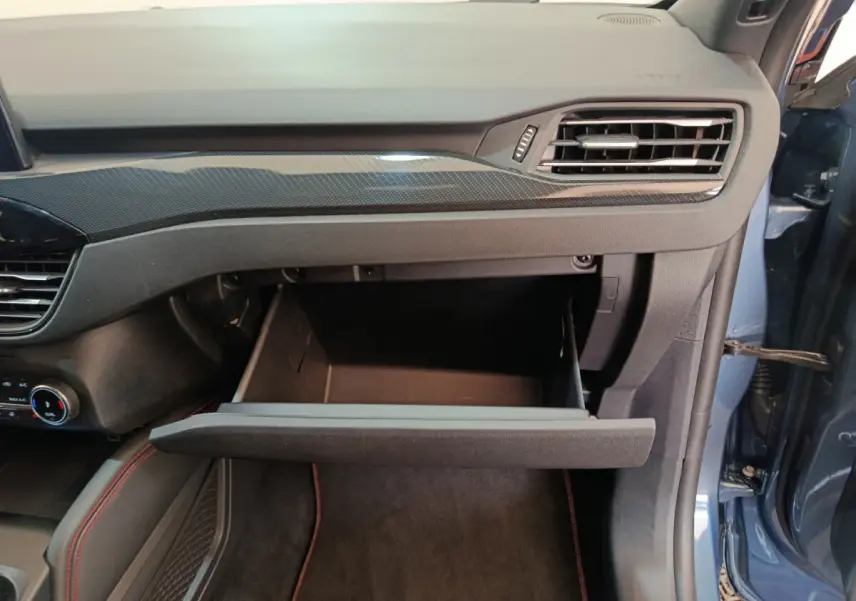 Vue intérieure côté passager du Ford Kuga bleu 2024, boîte à gants ouverte et tableau de bord noir avec insert carbone.