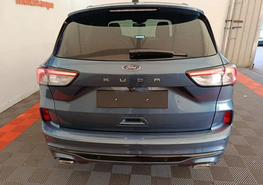 Vue arrière d'un Ford Kuga bleu 2024 avec feux LED et double sortie d'échappement dans un garage.