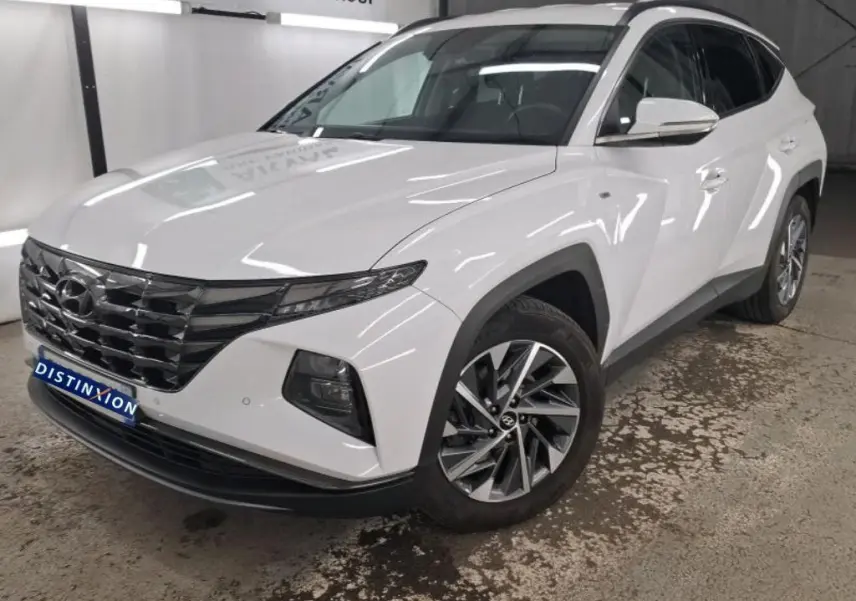 Hyundai Tucson blanc en 3/4 avant droit, avec jantes alliage et calandre chromée dans un showroom.