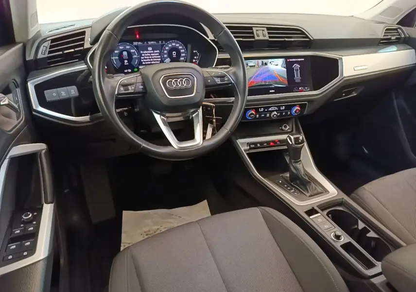 Intérieur Audi Q3 2023 vue avant du poste de conduite avec volant cuir noir et écran tactile central allumé.