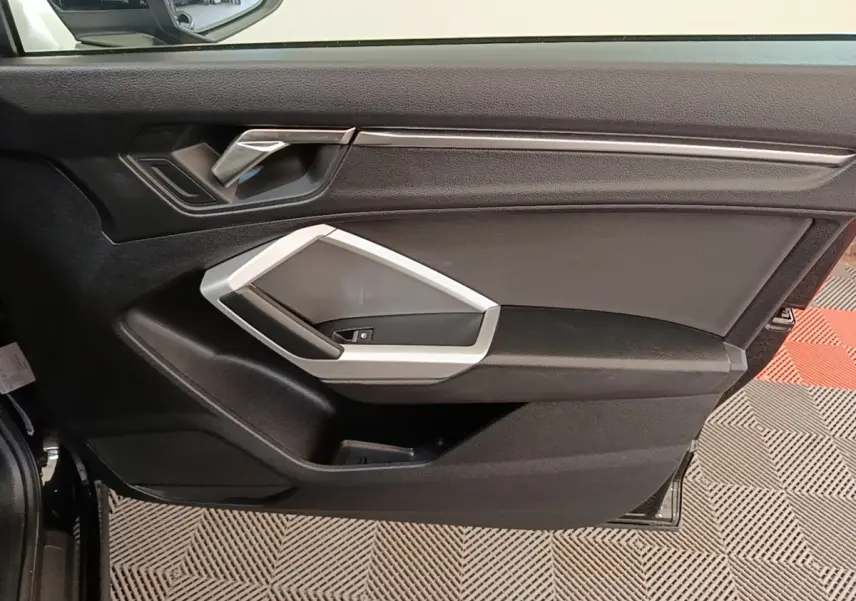 Vue intérieure côté gauche de la porte avant d’un Audi Q3 45 TFSI e 2023 avec garniture noire et insert argenté.