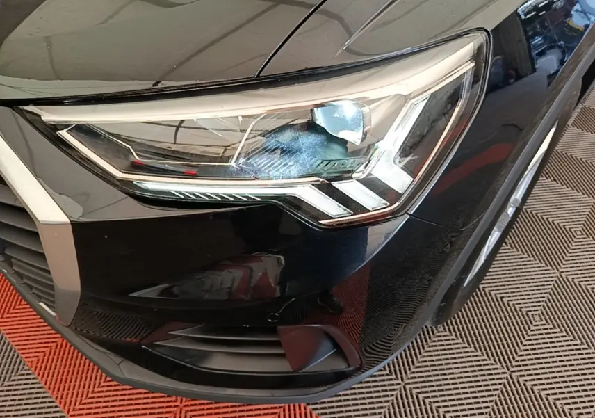 Gros plan sur le phare avant droit noir brillant de l’Audi Q3 45 TFSI e 2023 avec détails LED et calandre partielle.