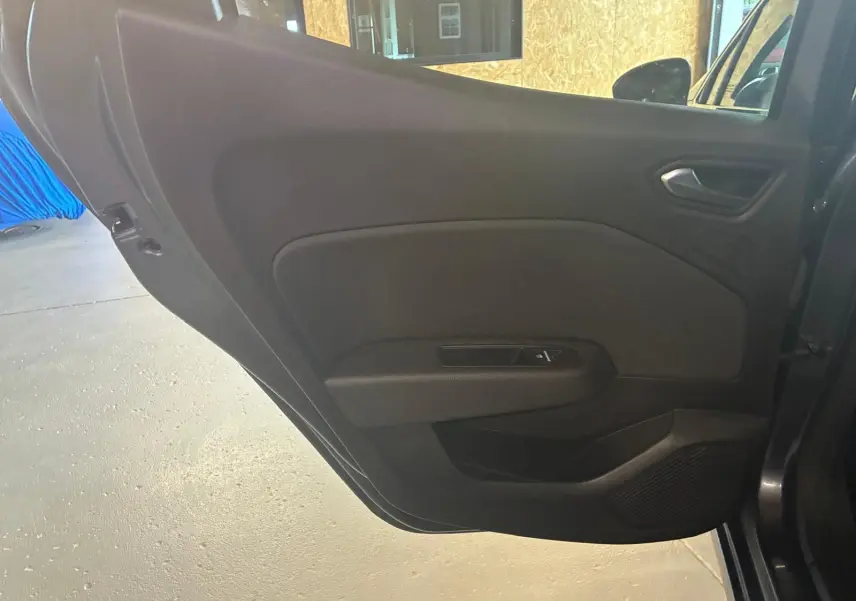 Gros plan sur la porte intérieure côté gauche d'une Renault Clio gris 2020, avec commande de vitre et tissu noir.