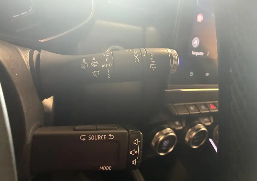 Gros plan sur les commandes au volant d'une Renault Clio gris 2020, avec boutons source et essuie-glace visibles.
