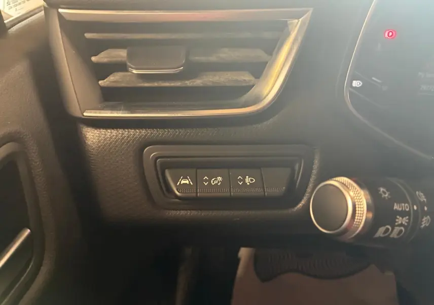 Gros plan sur les commandes d'assistance et de réglage des phares à gauche du volant dans l'habitacle gris-noir d'une Renault Clio 2020.