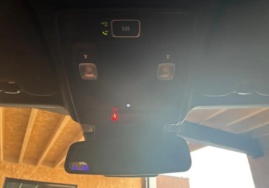 Vue intérieure du plafond avec boutons SOS et éclairages, rétroviseur et partie du toit en bois visible à l'extérieur.