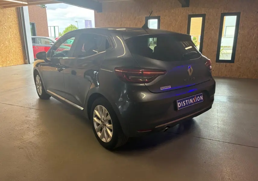 Renault Clio gris 3/4 arrière droit en intérieur, avec logo Renault et plaque Distinxion visible.