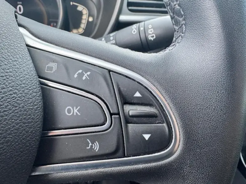Gros plan sur les commandes multifonctions du volant cuir du Renault Kadjar blanc, avec boutons de gestion d'appels et menu.