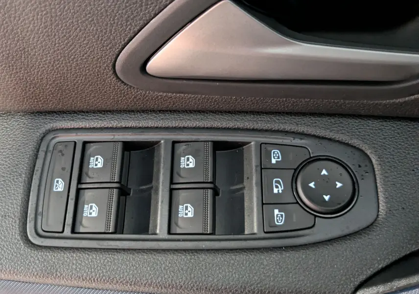 Gros plan sur les commandes des vitres électriques et des rétroviseurs sur la porte côté gauche du Dacia Duster blanc Glacier.