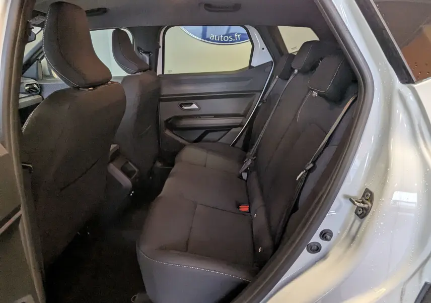 Vue intérieure côté droit sur la banquette arrière noire du Dacia Duster Hybrid 140 Journey blanc glacier 2025.