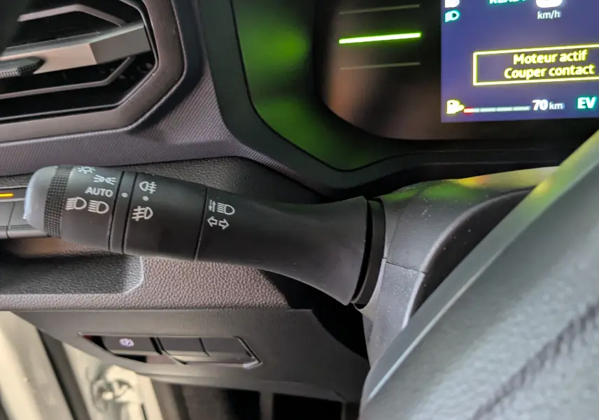 Gros plan sur la commande des phares à gauche du volant du Dacia Duster blanc glacier, tableau de bord numérique visible.