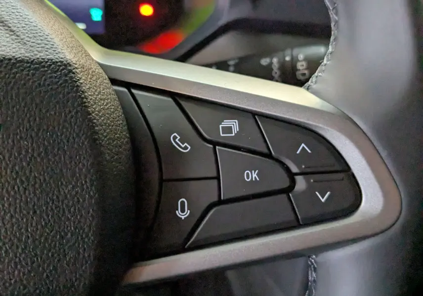 Gros plan sur les commandes multifonctions noires à droite du volant du Dacia Duster Hybrid 140 blanc glacier 2025.