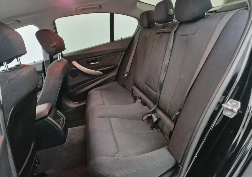Vue côté droit de l'intérieur arrière d'une BMW Série 3 316D noire, sièges tissu gris et ceintures de sécurité visibles.