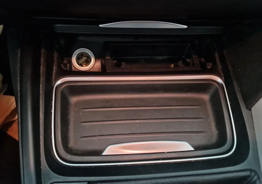 Gros plan sur le rangement central noir avec prise allume-cigare et bordure argentée dans une BMW Série 3 316D 2014.