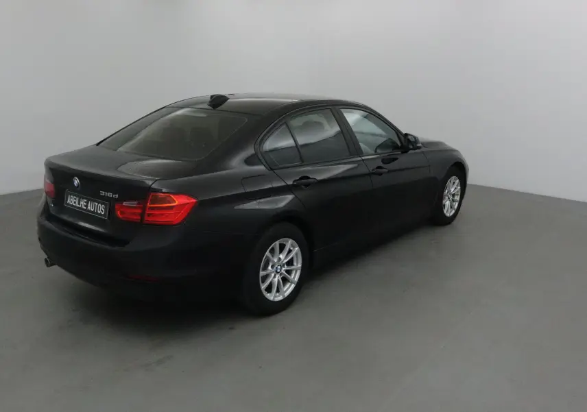 BMW Série 3 316d noire vue en 3/4 arrière droit, avec jantes alliage et feux arrière allumés.