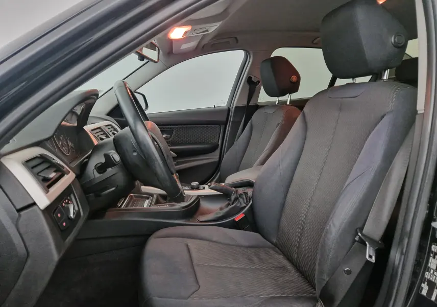 Vue intérieure côté conducteur de la BMW Série 3 316D noire, mettant en valeur les sièges tissu et la boîte manuelle.