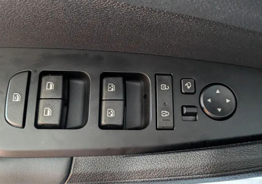 Gros plan sur les commandes de lève-vitres et rétroviseurs du côté gauche intérieur d’un Kia Sportage blanc.