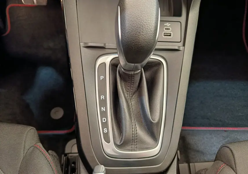 Gros plan sur la console centrale de la Ford Puma bleue, montrant le levier de vitesses automatique en cuir noir avec surpiqûres rouges.