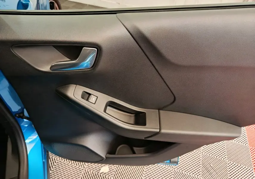 Vue intérieure du panneau de porte côté gauche bleu du Ford Puma 2025 avec poignée argentée et commande de vitre.