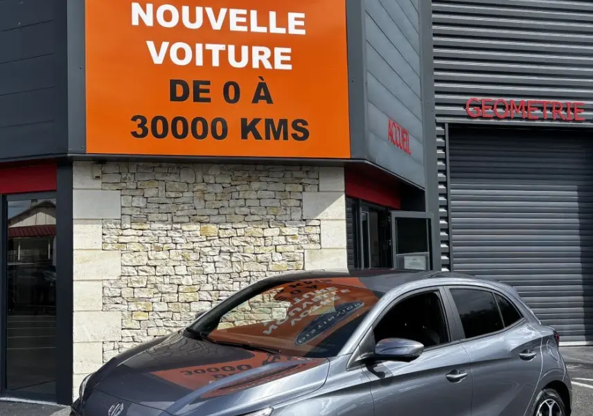 MG3 1.5L Hybrid+ Luxury gris clair vu en 3/4 avant droit devant un bâtiment commercial.