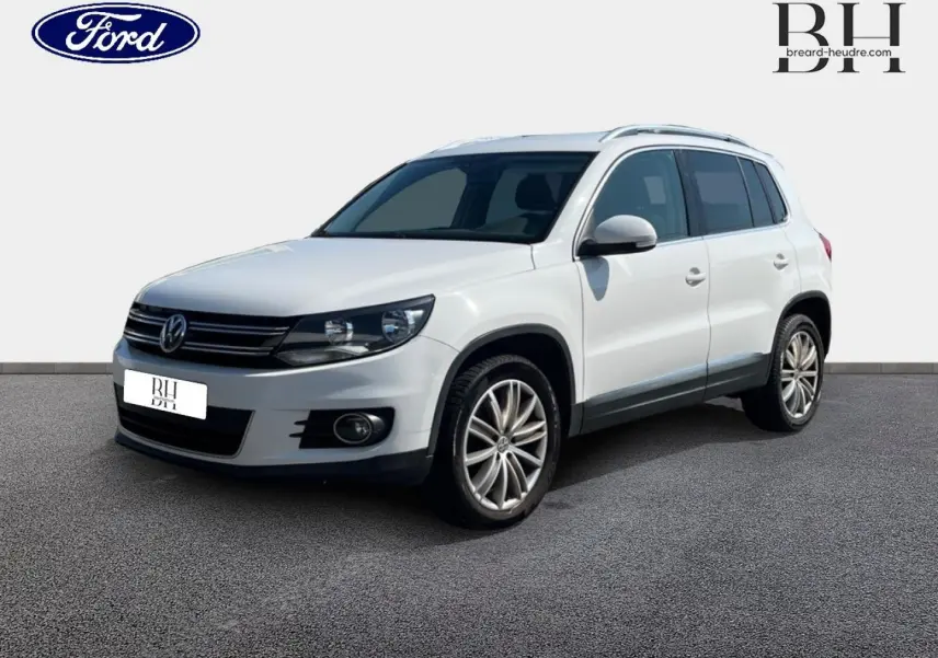 Volkswagen Tiguan blanc Candy en 3/4 avant droit, avec jantes alliage et barres de toit visibles.