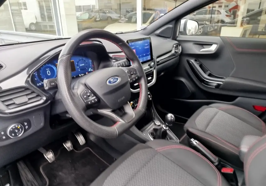 Intérieur avant droit du Ford Puma 1.0 EcoBoost 2021 avec volant cuir perforé et surpiqûres rouges, console tactile visible.