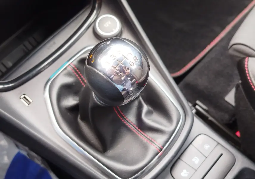 Gros plan sur le levier de vitesses manuel chromé avec coutures rouges dans l'habitacle gris du Ford Puma 2021.