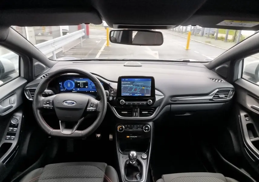 Vue intérieure avant du Ford Puma 1.0 EcoBoost 2021, tableau de bord noir avec écran tactile et volant multifonction.