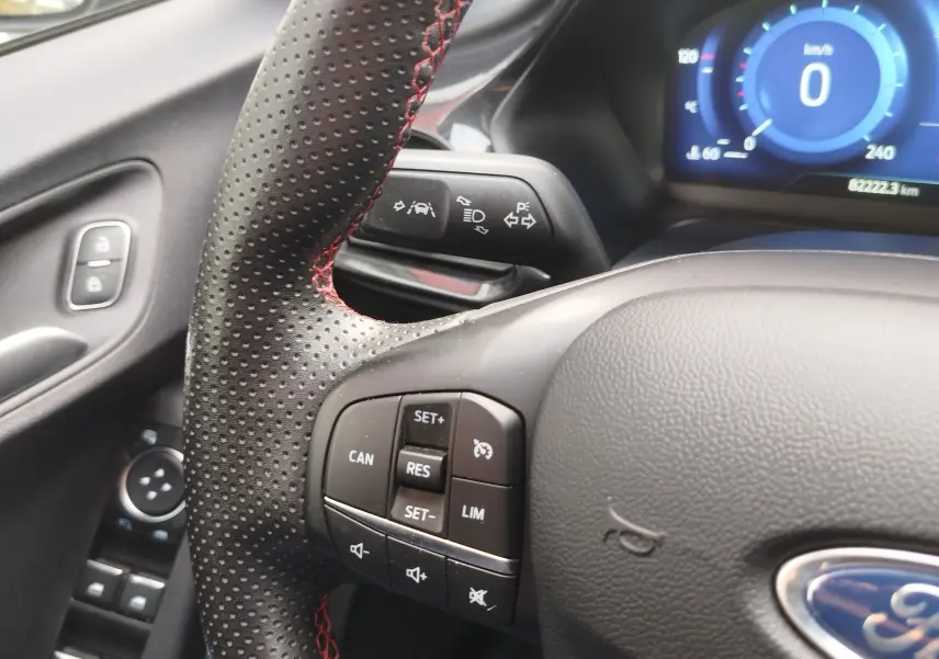 Gros plan sur le volant perforé avec surpiqûres rouges et commandes multifonctions du Ford Puma 2021 intérieur gris.