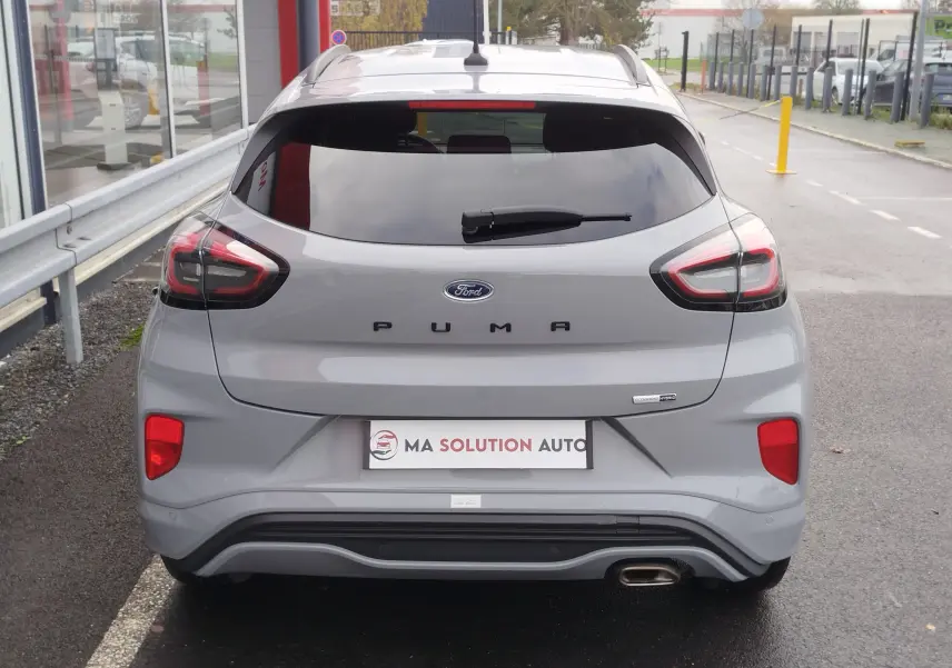 Vue arrière d'une Ford Puma 1.0 EcoBoost gris mat avec feux LED et sortie d'échappement visible sur un parking.
