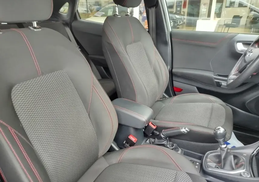 Intérieur avant du Ford Puma 1.0 EcoBoost 2021, sièges tissu gris avec surpiqûres rouges et boîte manuelle visible.