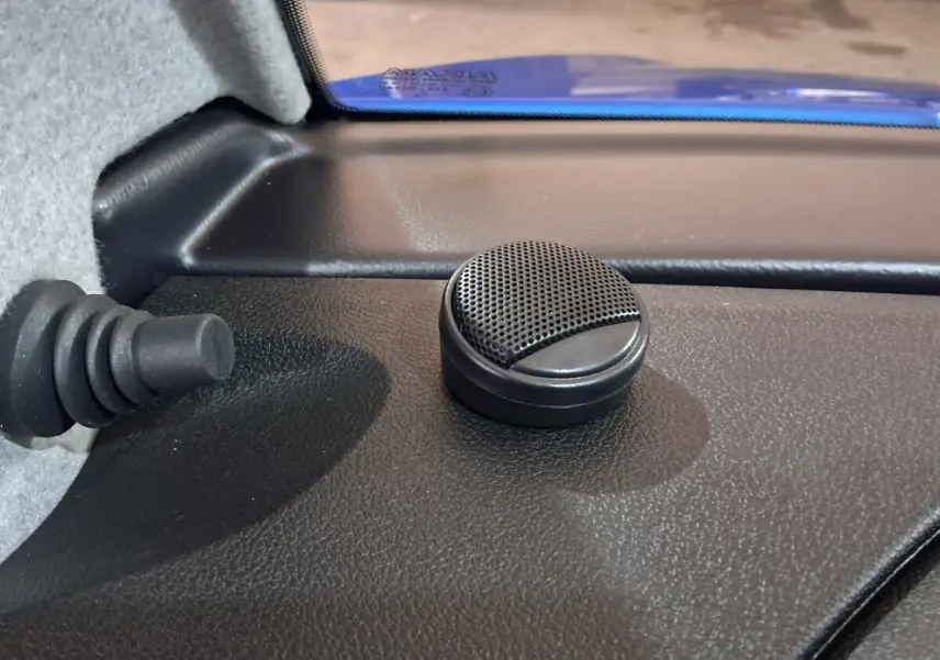 Gros plan sur un haut-parleur rond noir à l'intérieur d'une Aixam Ambition bleu, côté conducteur, près du pare-brise.