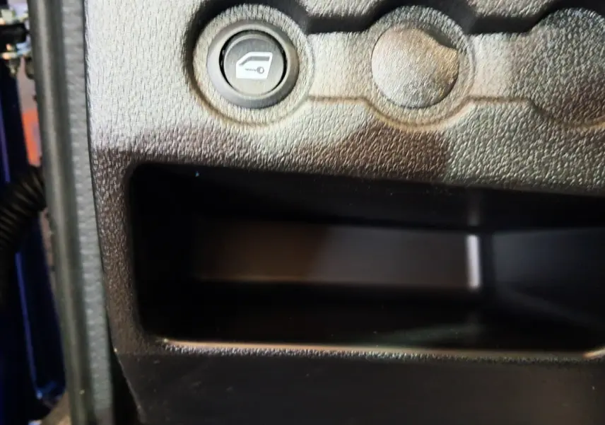 Gros plan sur le bouton d'ouverture du coffre côté conducteur dans l'habitacle d'une Aixam Ambition bleu.