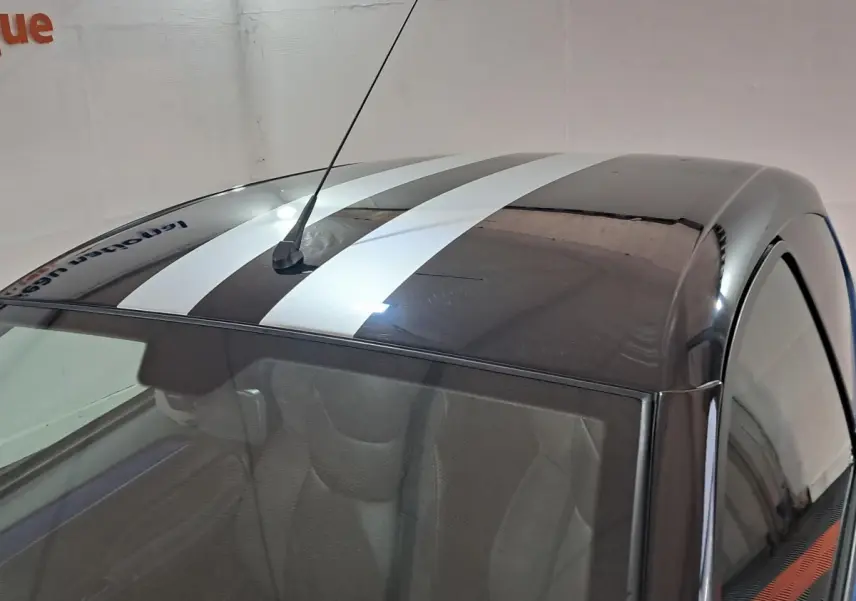 Vue plongeante sur le toit noir à bandes blanches d'une Aixam Ambition bleu, avec antenne centrale visible.