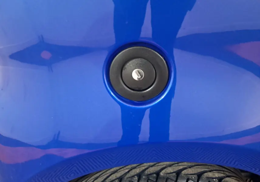 Gros plan sur la serrure de la trappe à carburant d'une Aixam Ambition bleu, avec partie de pneu visible en bas.