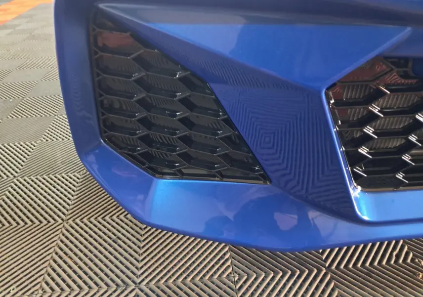 Gros plan sur la calandre avant droite bleu métallisé de l'AIXAM AMBITION 0.5 CITY GTO avec motif nid d'abeille noir.