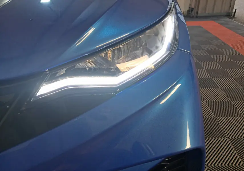 Gros plan sur le phare avant droit bleu métallisé de l'AIXAM AMBITION 0.5 CITY GTO avec éclairage LED allumé.