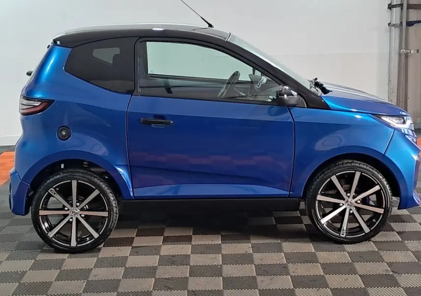 Vue de profil côté gauche d'une Aixam Ambition 2026 bleu avec jantes noires et rétroviseur caméra côté conducteur.