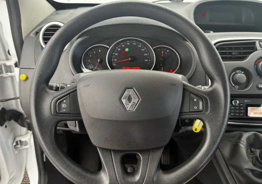 Vue rapprochée du volant noir multifonctions d’un Renault Kangoo blanc, tableau de bord et levier de vitesse visibles.