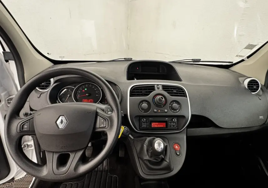 Vue intérieure avant du tableau de bord et volant noir d’un Renault Kangoo blanc de 2016 avec boîte manuelle.