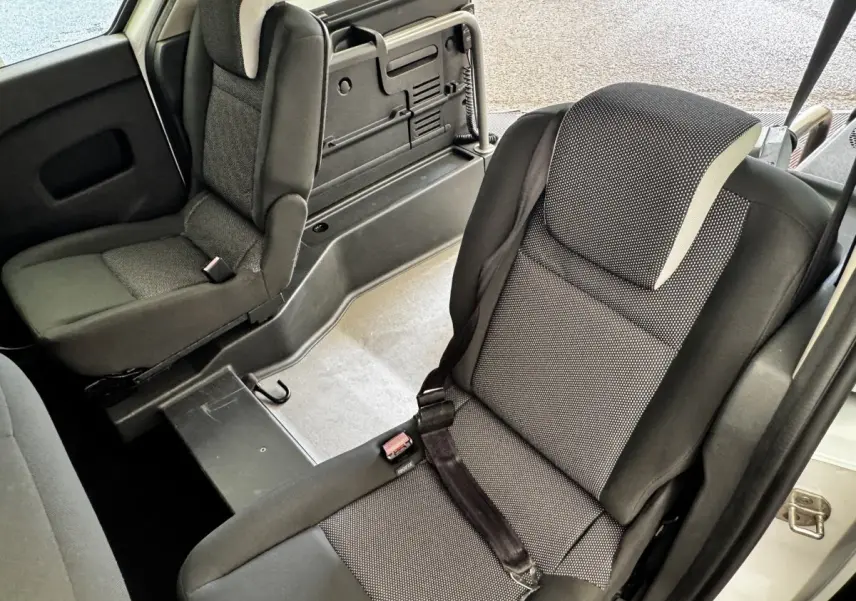 Vue intérieure sur les sièges arrière gris foncé du Renault Kangoo Zen blanc, avec banquette fractionnée et ceinture de sécurité.