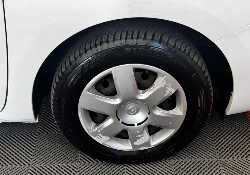 Gros plan sur la roue avant droite blanche d’un Renault Kangoo 2016 avec enjoliveur abîmé et pneu Firestone.