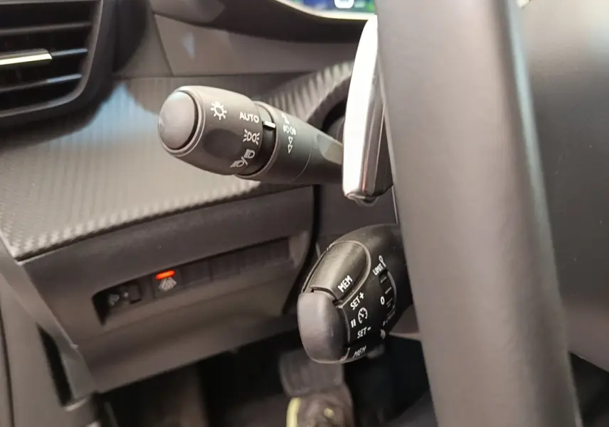 Gros plan sur les commandes de régulateur de vitesse et des phares à gauche du volant d’un Peugeot 2008 blanc, intérieur noir.