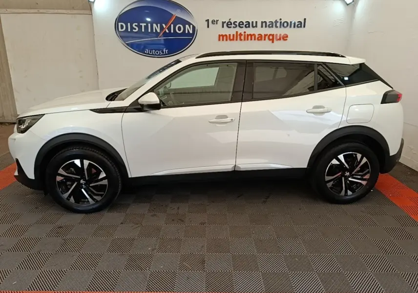 Vue latérale droite d'un Peugeot 2008 blanc 2021 avec jantes noires et toit noir contrasté en intérieur showroom.